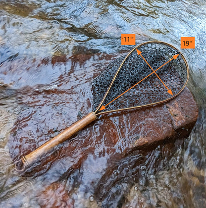 A bamboo fly fishing net lying on a rock in the water on the river in Western North Carolina. The rubber net basket is smooth and shiny and protects the fish for catch and release. The handle is flame cured for strength and durability and there is copper stitching and a copper keeper ring to attach your net keeper to.