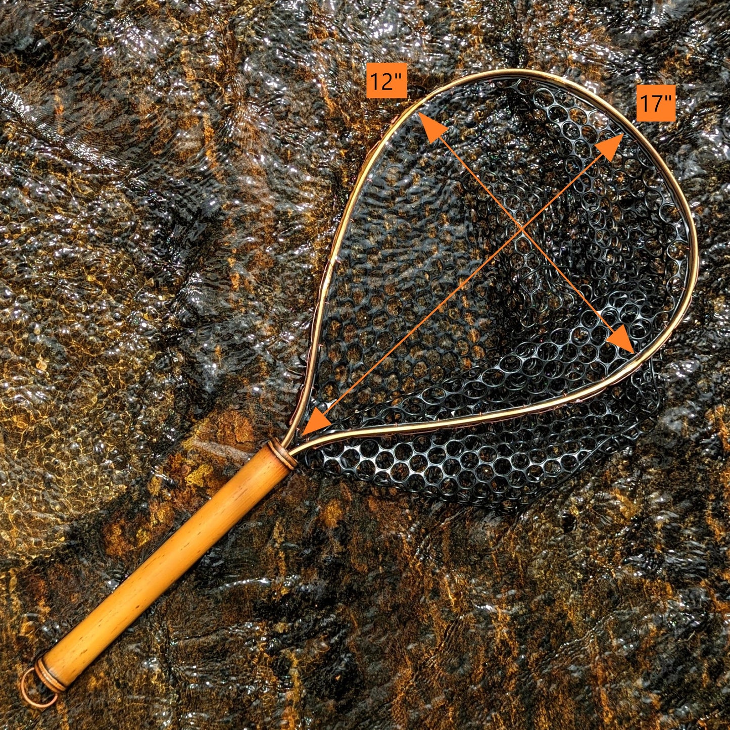 A bamboo fly fishing net lying on a rock in the water on the river in Western North Carolina. The rubber net basket is smooth and shiny and protects the fish for catch and release. The handle is flame cured for strength and durability and there is copper stitching and a copper keeper ring to attach your net keeper to.